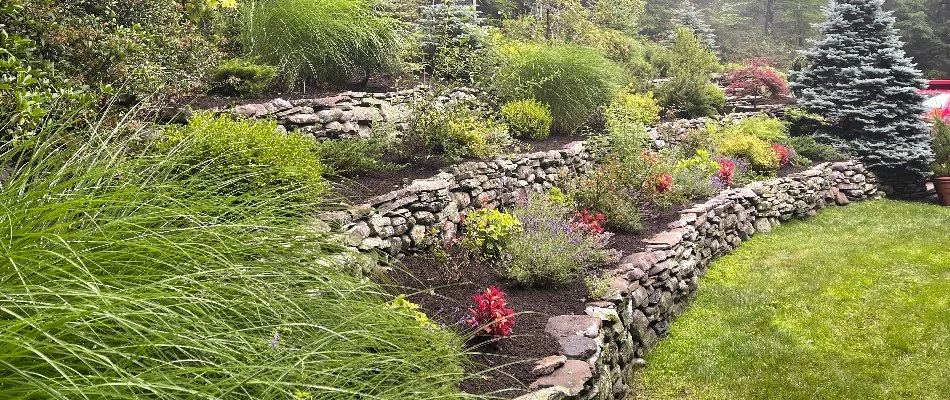 A three-tier retaining wall in Alpine, NJ, with shrubs and flowers.